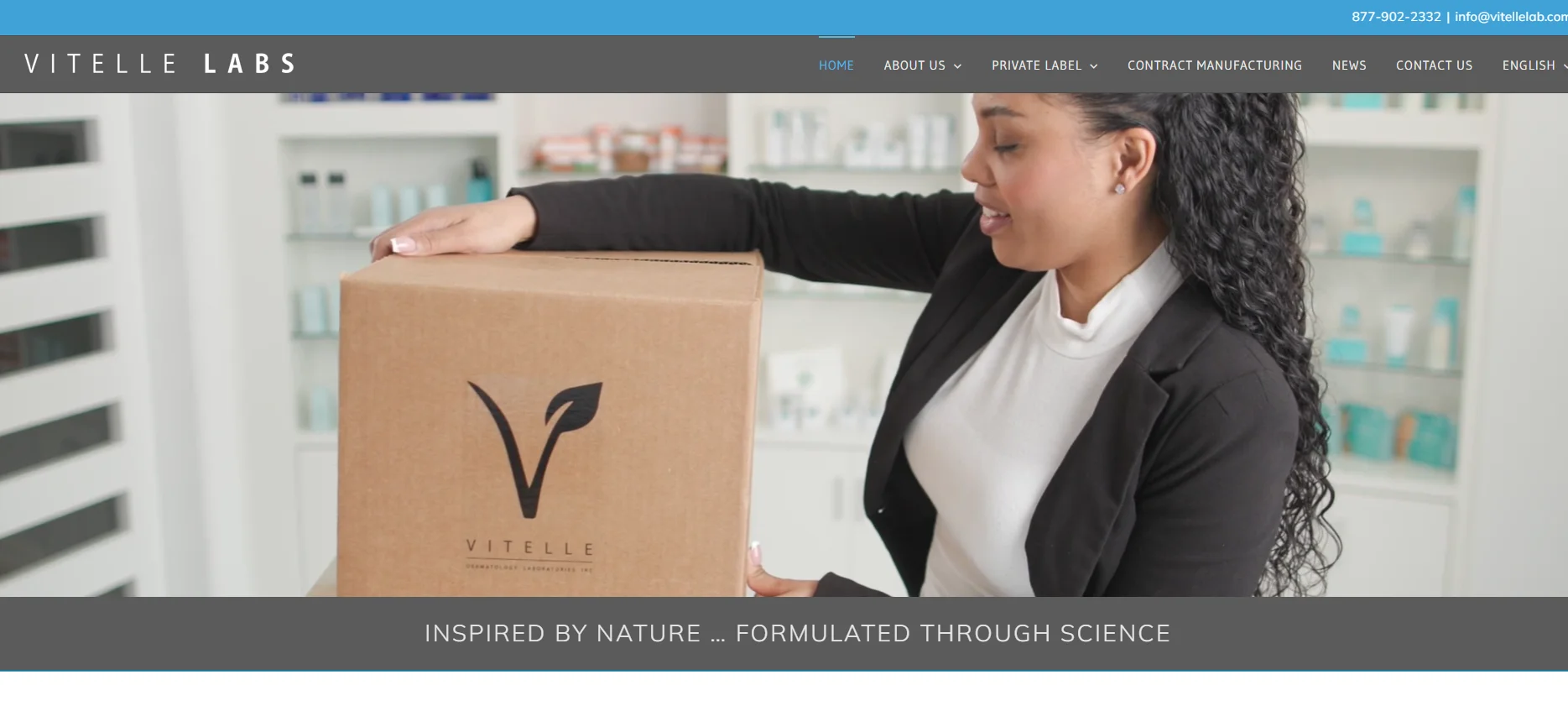 A woman holding a Vitelle Labs branded cardboard box in a laboratory setting with skincare products in the background.